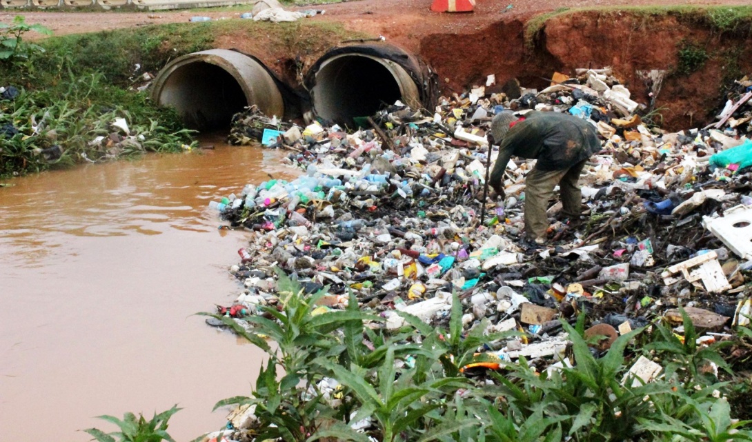A young man picks up plastics from a water channel along Northern bypass in Kampala Uganda, East Africa. Due to poor solid waste management, with a collection of garbage and dumped plastic bottles collects in water channels and sometimes leading to floods. Photo by Davidson Ndyabahika.